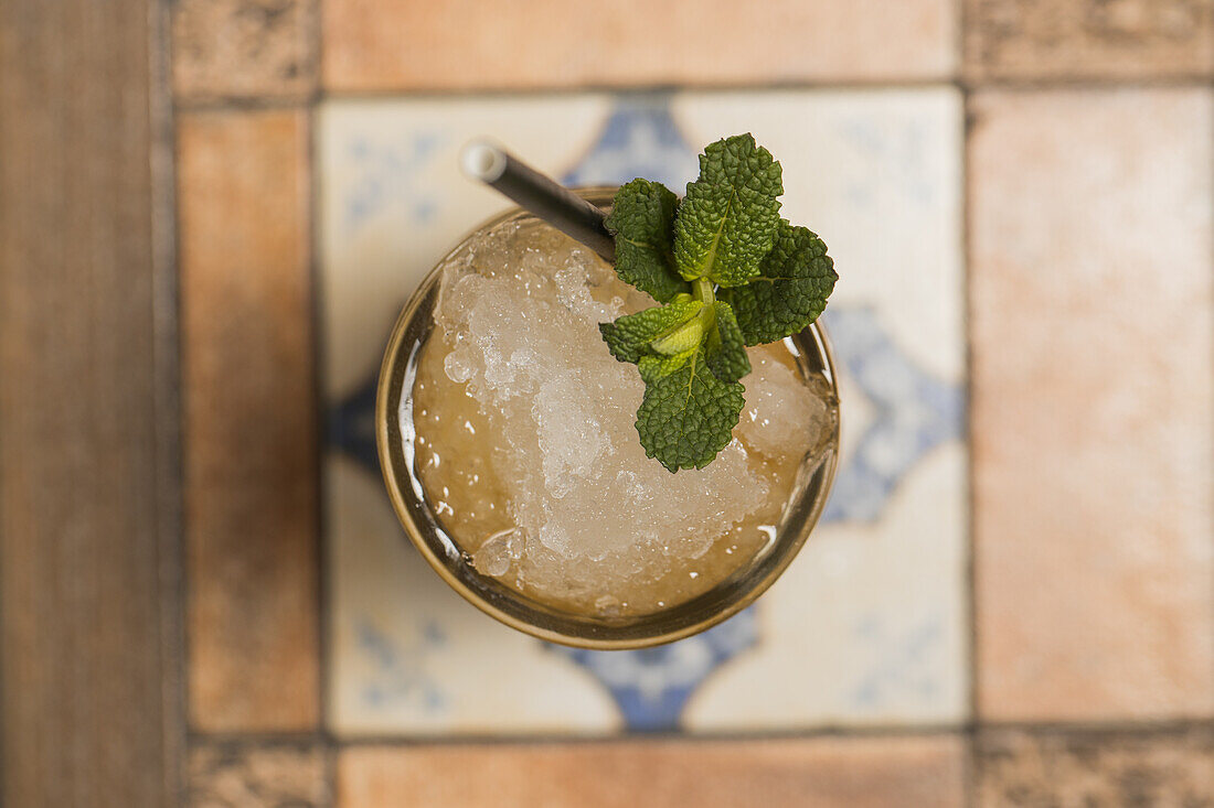 Von oben auf Tiki-Becher mit kaltem Alkoholgetränk mit Strohhalm, serviert mit Eis und dekoriert mit frischem Kraut auf unscharfem Hintergrund