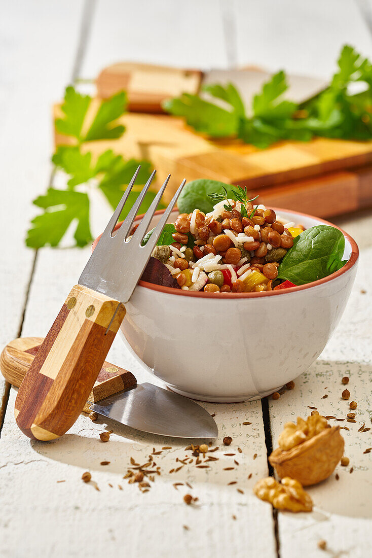 Keramikschüssel mit Salat aus verschiedenen Nüssen und Gemüse mit Grünzeug auf einer weißen Holzbank mit Messer und Gabel
