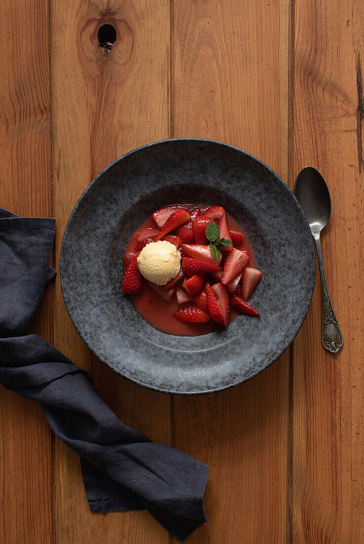 Draufsicht auf leckere flambierte Erdbeerhälften mit Vanilleeis in einem Teller auf einem Holztisch