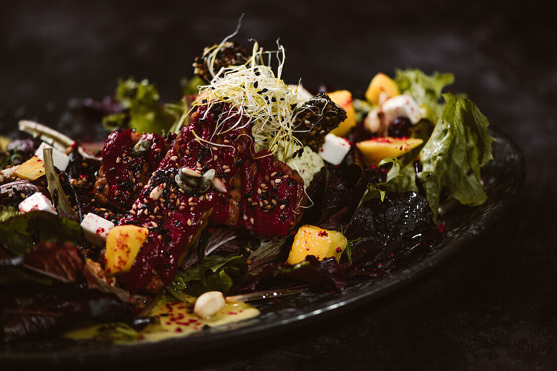 Plate with tasty vegetarian Indonesian salad with fresh mango and cashew cheese slices near soybeans and condiments covered with basil vinaigrette