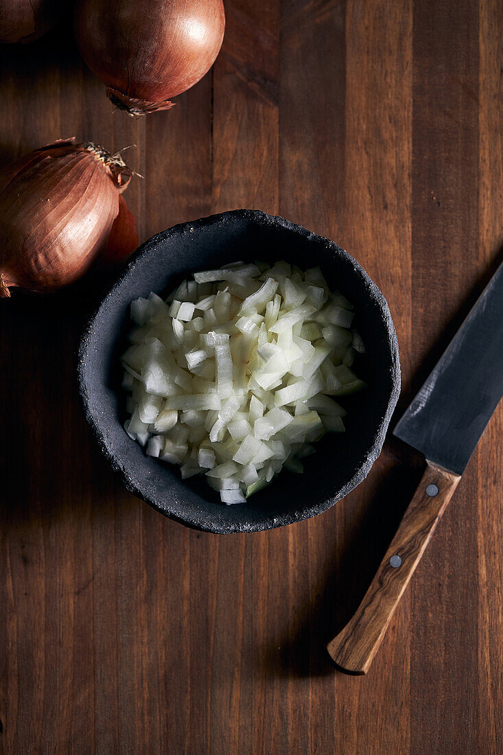 Top view of rustic bowl with pieces of cut onion placed near knife on lumber table in kitchen