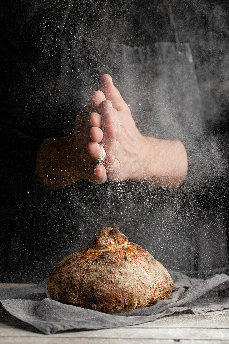 Unbekannter Koch in Schürze steht am Tisch und verziert einen Laib traditionelles Brot mit Mehl