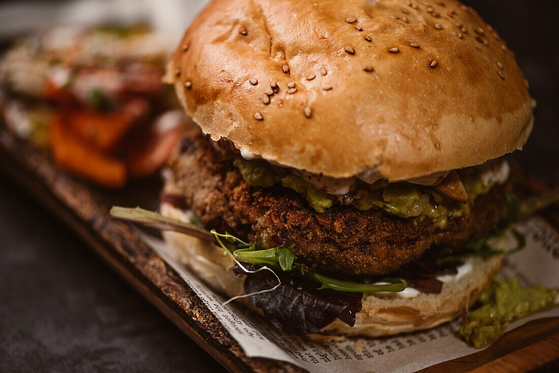 Nahaufnahme eines leckeren Burgers mit vegetarischer Frikadelle und gegrillten Shiitakes zwischen Brötchen neben Süßkartoffel- und Karottenscheiben mit Alioli-Sauce auf dunklem Hintergrund