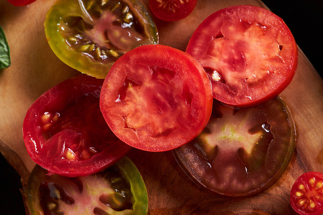 Hochformatige geschnittene Tomate mit Salz auf einem hölzernen Schneidebrett zwischen reifen roten Tomaten mit Wassertropfen