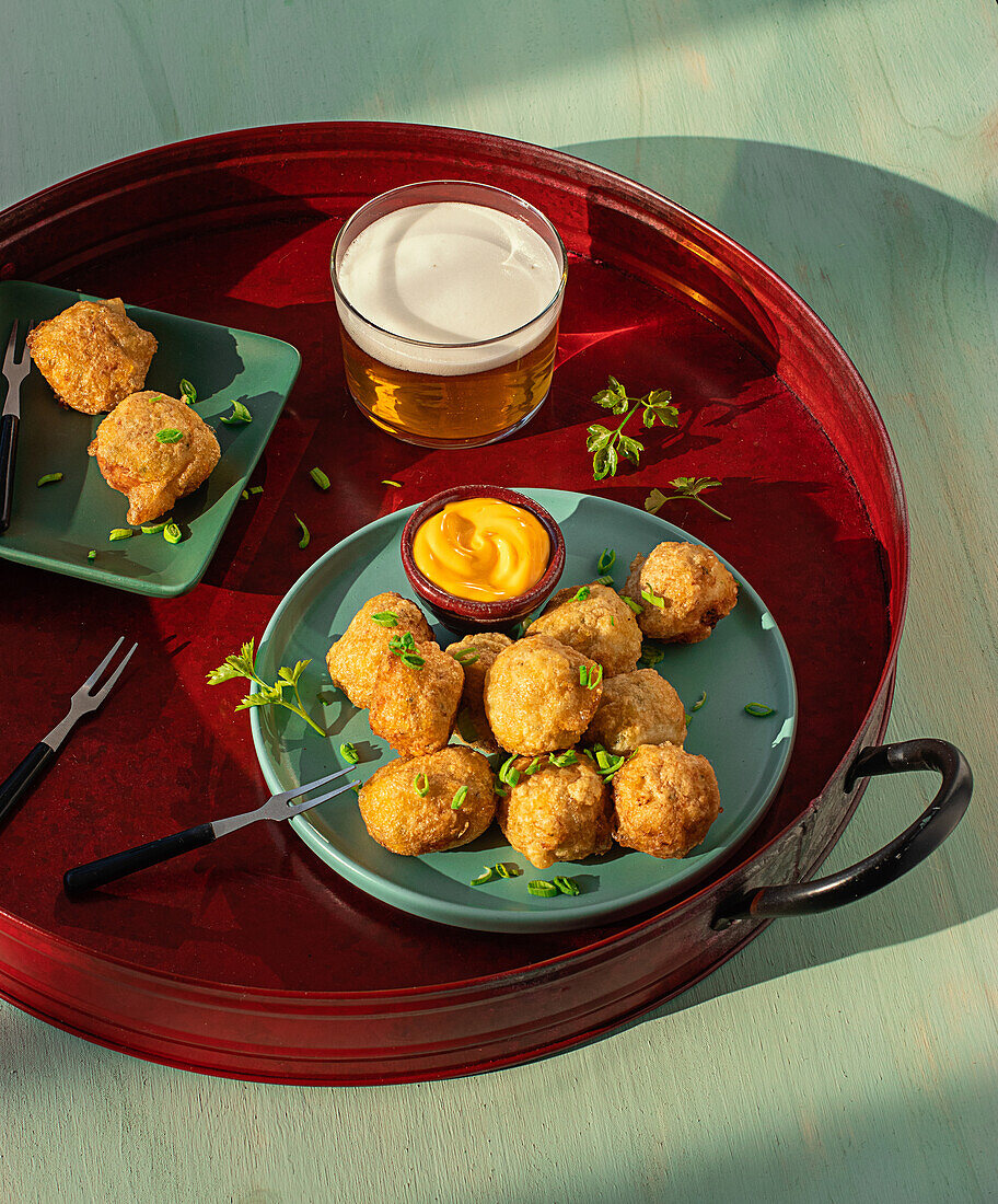 From above traditional codfish fritters server on tray with fresh herbs and glass of beer on green background