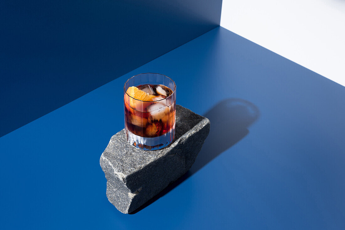 from above glass of alcoholic cocktail made with red vermouth served with orange slices on stone in light studio with blue and white wall