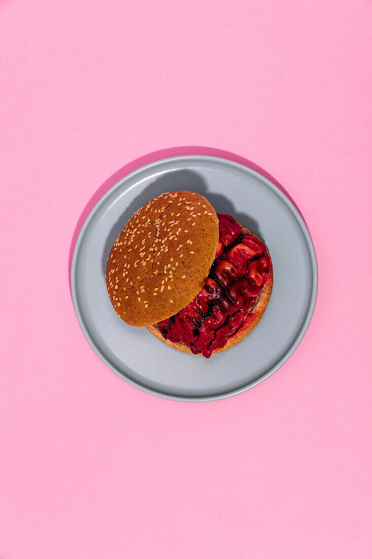 Burger mit blutigem Gehirn und Brötchen mit Sesam von oben auf grauem Teller auf rosa Hintergrund serviert