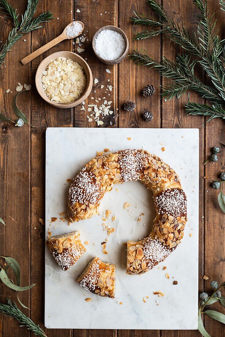 Overhead view of tasty three kings cake decorated with almond petals and coconut flakes among Eucalyptus and fir sprigs