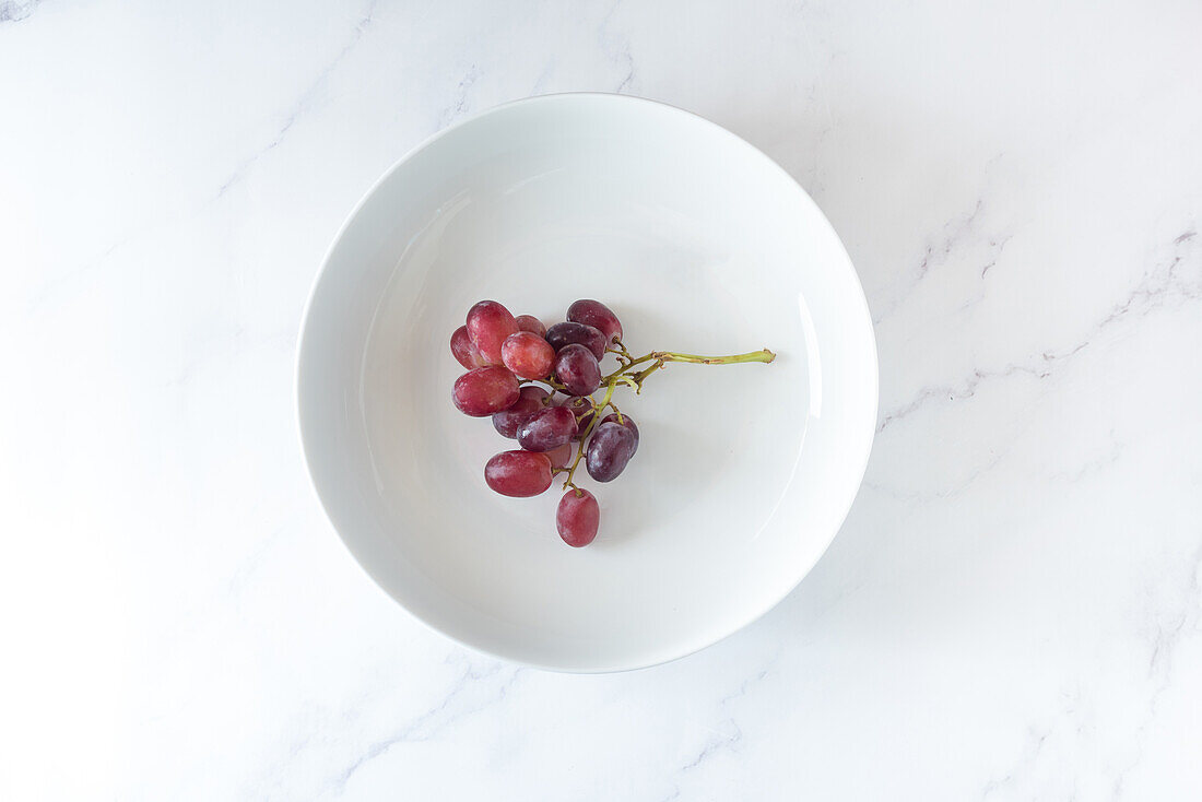 From above of bunch of sweet pink grape served on plate on white background