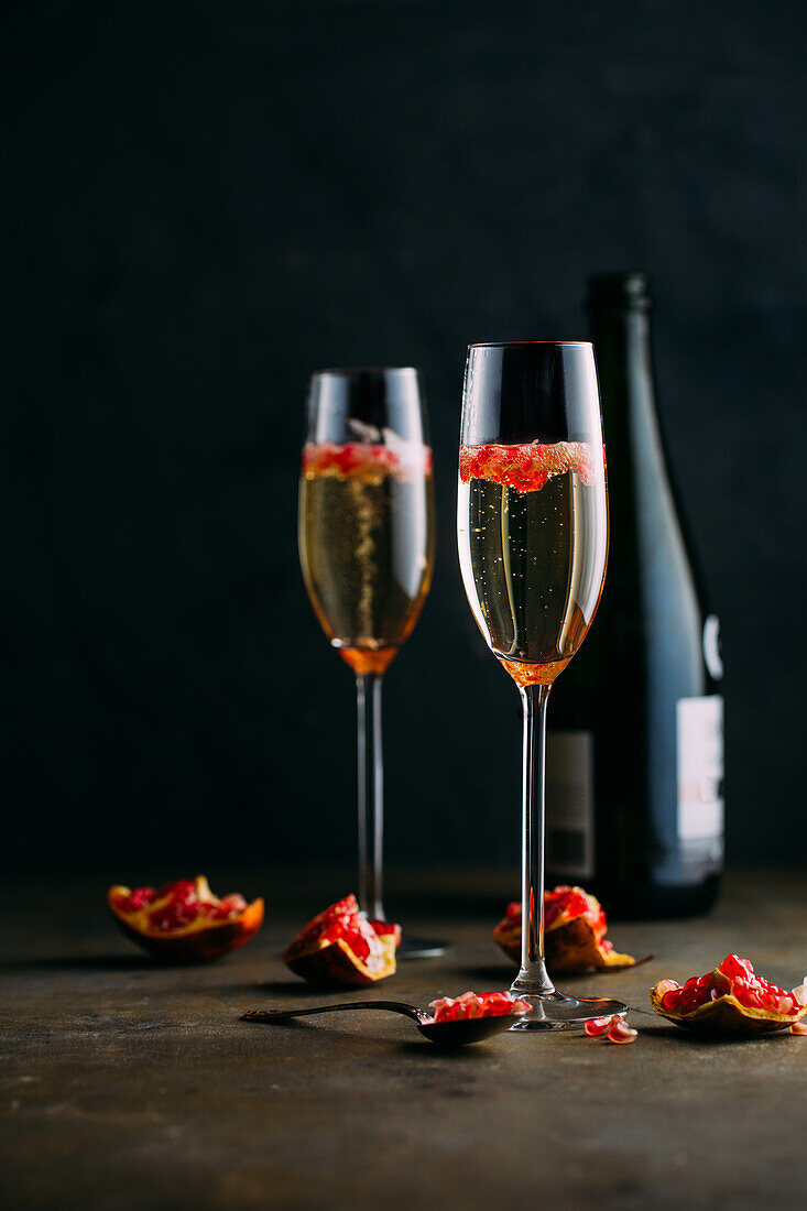 Champagne cocktail with pomegranate placed on rustic surface against dark background