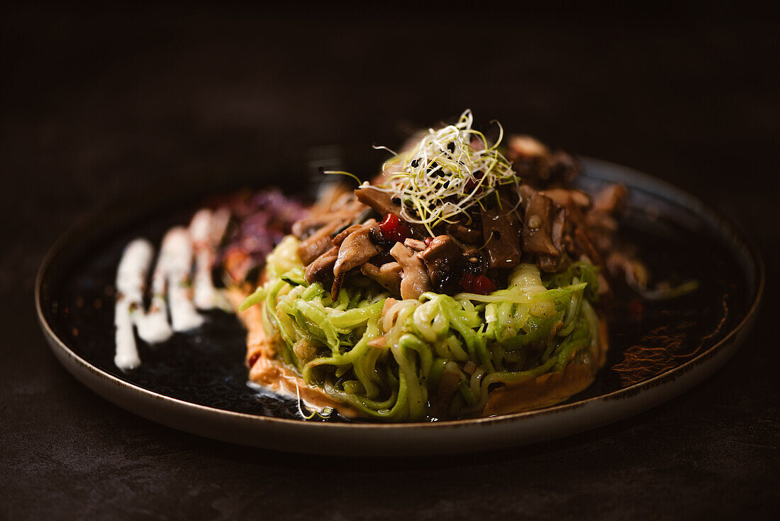 Yummy vegan dish with zucchini spaghetti and sauteed mushroom slices covered with red berries and alfalfa sprouts on dark background