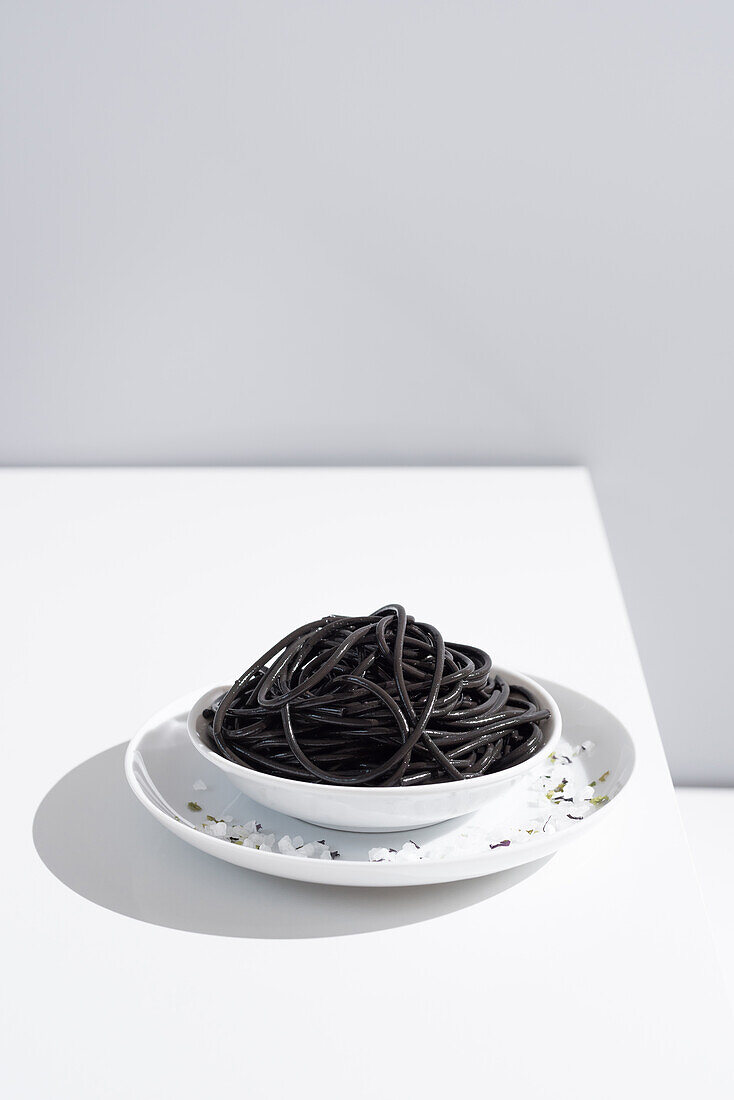 Minimalist studio with black squid ink spaghetti in full ceramic bowl on white table