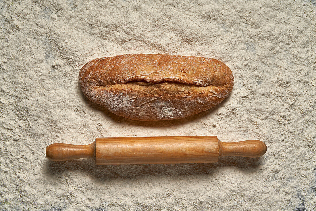 Draufsicht Vollbild Laib frisch gebackenes Brot mit hölzernem Nudelholz auf weißem Mehl in hellem Raum platziert