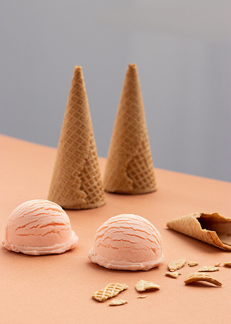 Pink ice cream scoop and waffle cones placed on table in studio