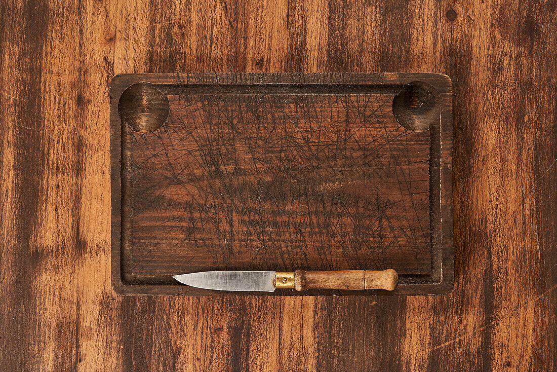 From above scratched chopping board with sharp knife placed on rustic lumber table