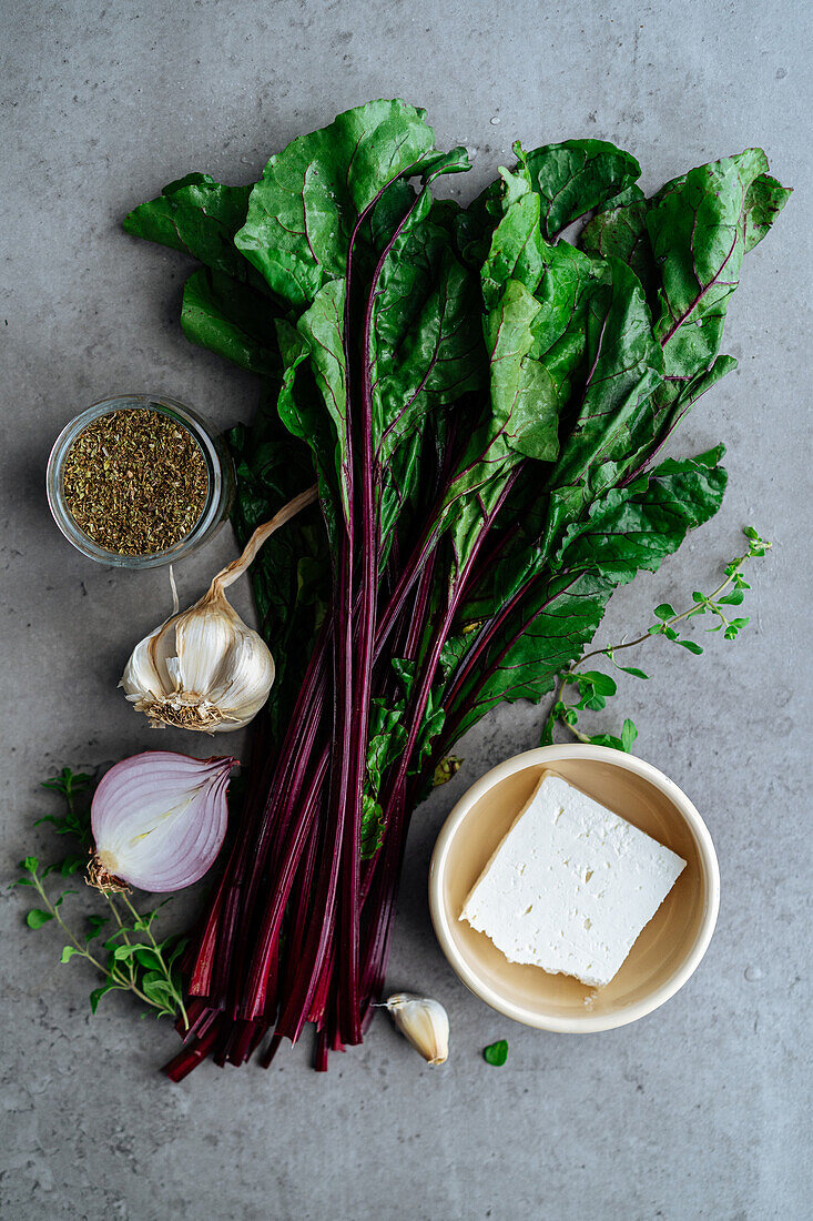 Top view of fresh beetroot leaves with feta cheese for pie on gray background with seasoning and onion in kitchen