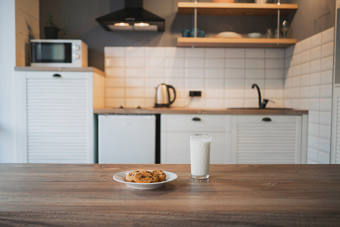 Plate with tasty oatmeal biscuits with chocolate chips against glass of milk on wooden table
