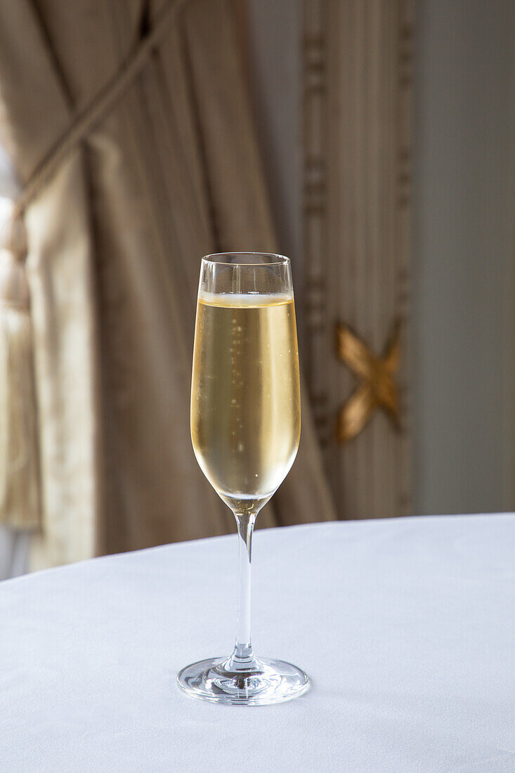 Crystal glass of sparkling wine served on white round table in elegant restaurant in daylight