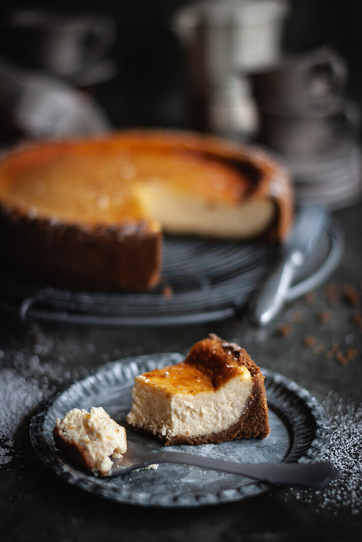 From above of piece of sweet tasty appetizing cheesecake served on plate with spoon on gray table near pie placed on baking pan with knife