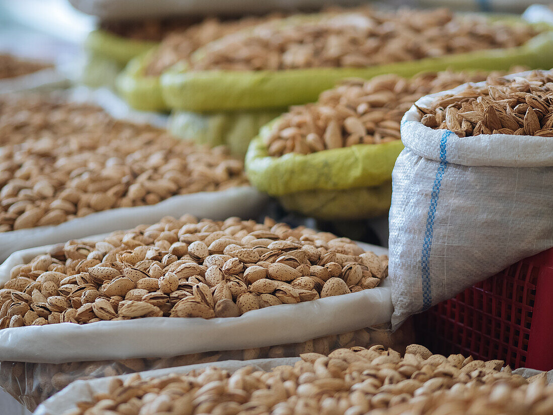 Pile of delicious pistachios placed in plastic bags on stall with various types of nuts in market