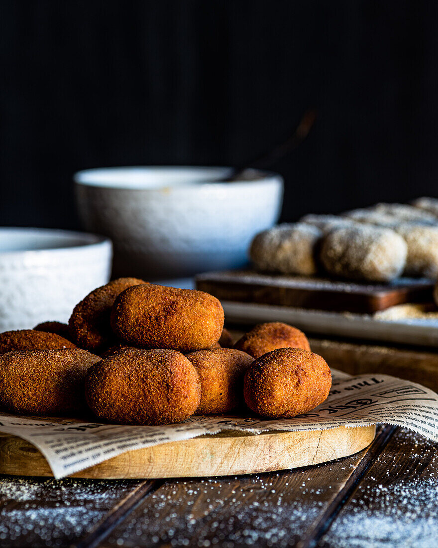 Delicious fried croquettes rolled in bread crumbs placed on piece of newspaper on wooden board