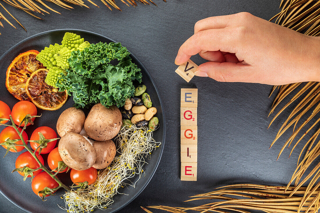 Anonyme Köchin von oben, die einen dekorativen Titel neben verschiedenen Gemüsesorten und Früchten mit Nüssen auf einem Teller auf grauem Hintergrund zusammenstellt