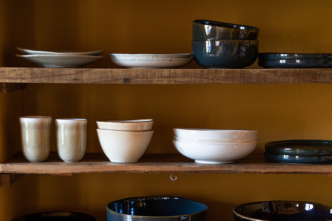 Set von verschiedenem Geschirr, bestehend aus Tellern, Tassen und Schüsseln, auf Holzregalen