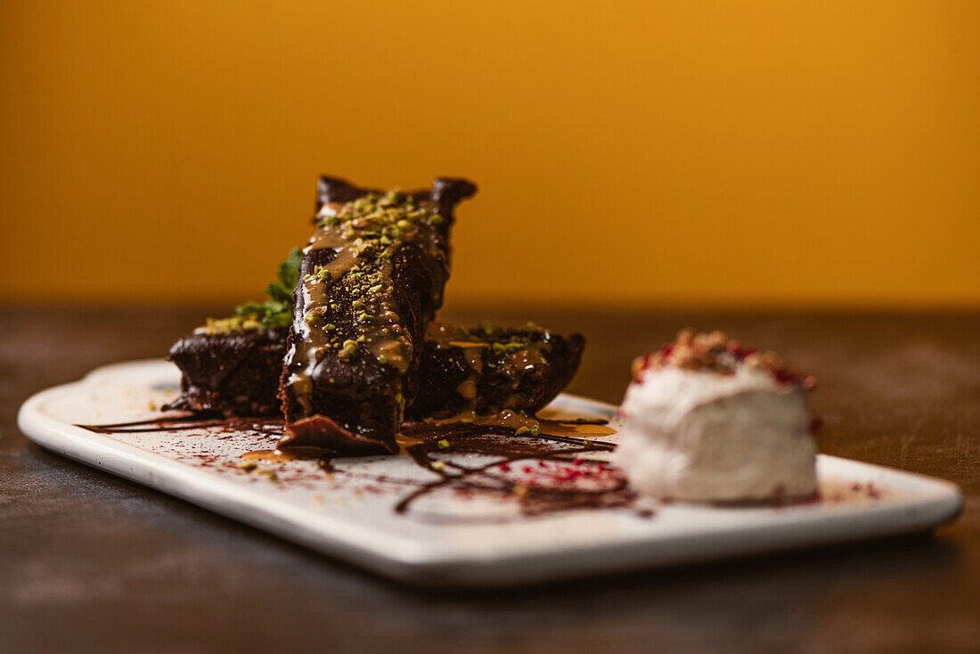 Leckere Brownies mit Erdnussbutter und knusprigen, zerstoßenen Pistazien neben einer Kugel Gelato auf einem Teller mit Schokoladensauce