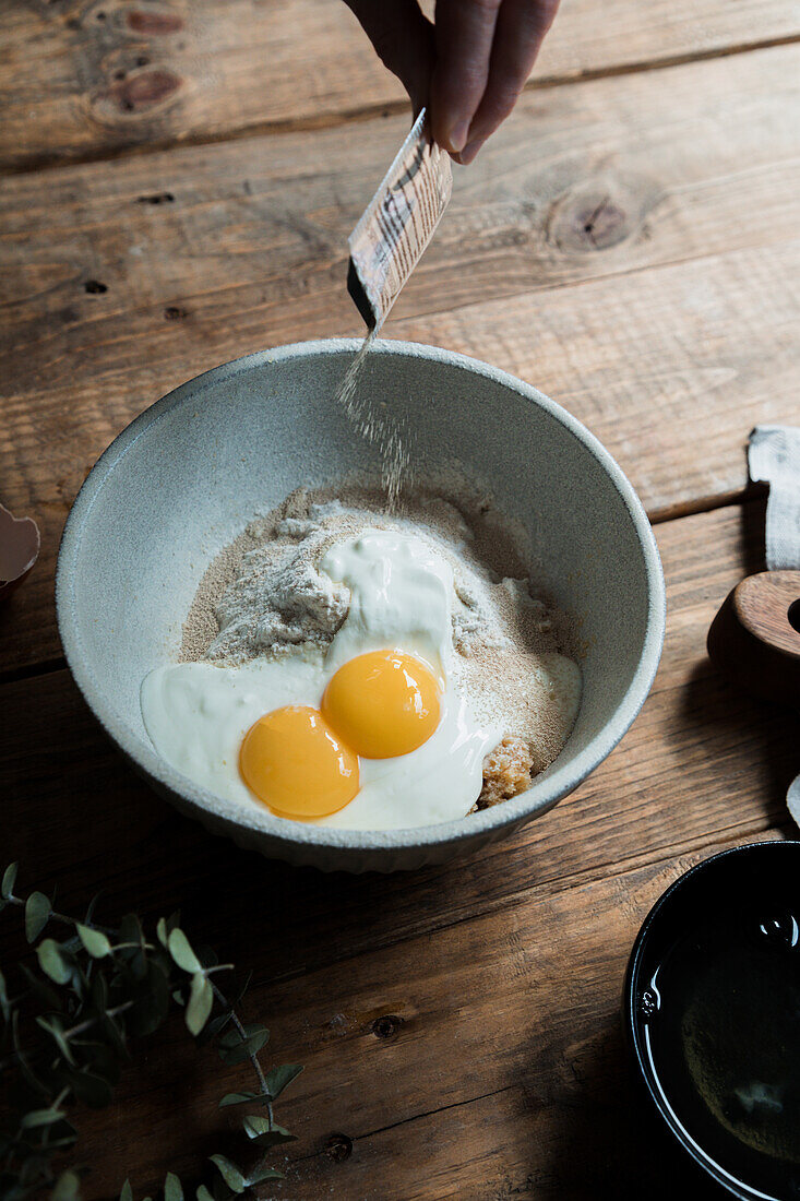 Schüssel mit Eiern und Sahne, vermischt mit Semmelbröseln und Mehl auf einem Holztisch bei der Zubereitung von Gebäck von oben