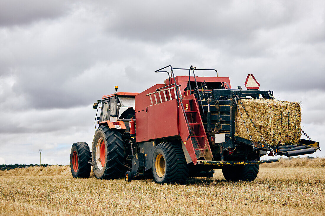 Getrocknete Heurolle und moderner Traktor auf landwirtschaftlichem Feld in bergigem Gebiet im Sommer