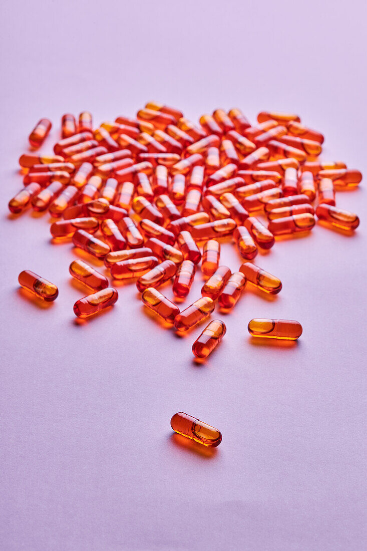 Komposition von orangefarbenen Pillen auf rosa Hintergrund in einem hellen Studio verstreut