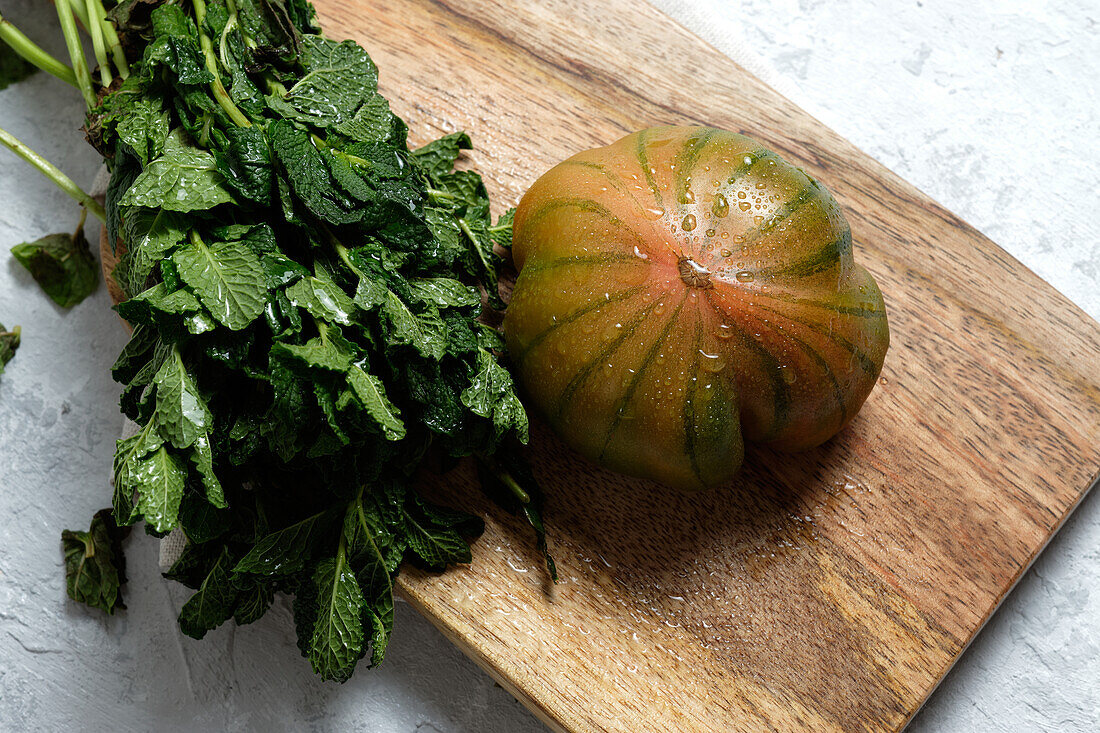 Frische gestreifte grüne und rote Tomaten auf einem Holzbrett mit Minzstängeln