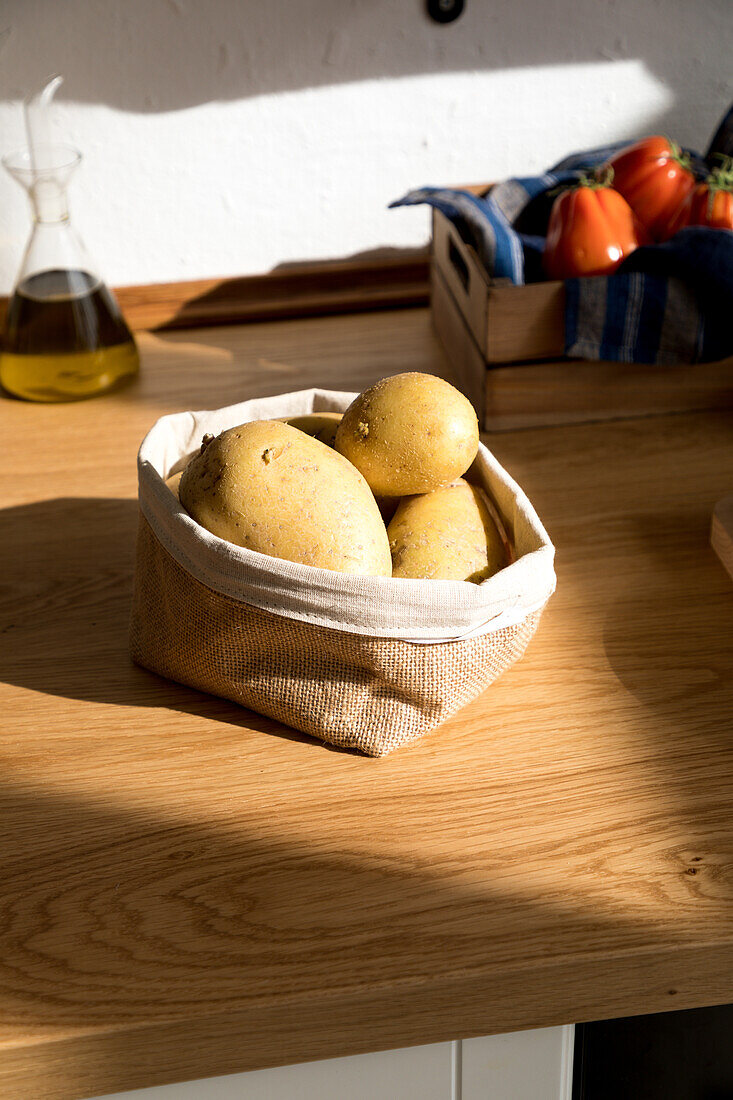 Hoher Winkel eines Bündels roher gelber Kartoffeln in einem Stoffsack auf einem Holztisch mit Zutaten für die Zubereitung von Speisen in der heimischen Küche