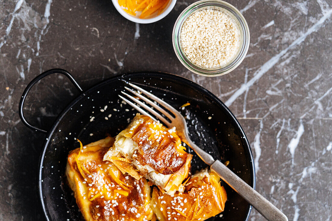 Top view of sweet tasty pastry with sesame seeds served on black plate with fork in light kitchen