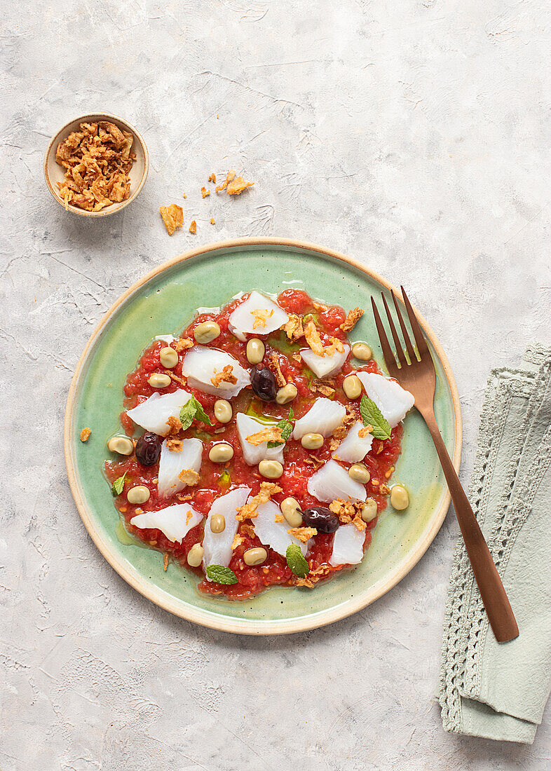 Summery tomato and cod salad in a shallow dish with a fork and a bowl of fried onions