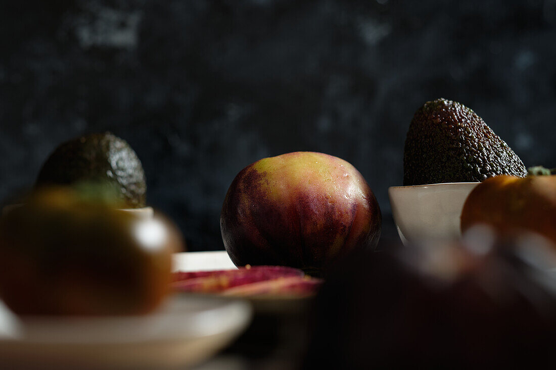 Fresh whole and sliced black tomatoes on table with avocado during healthy meal preparation