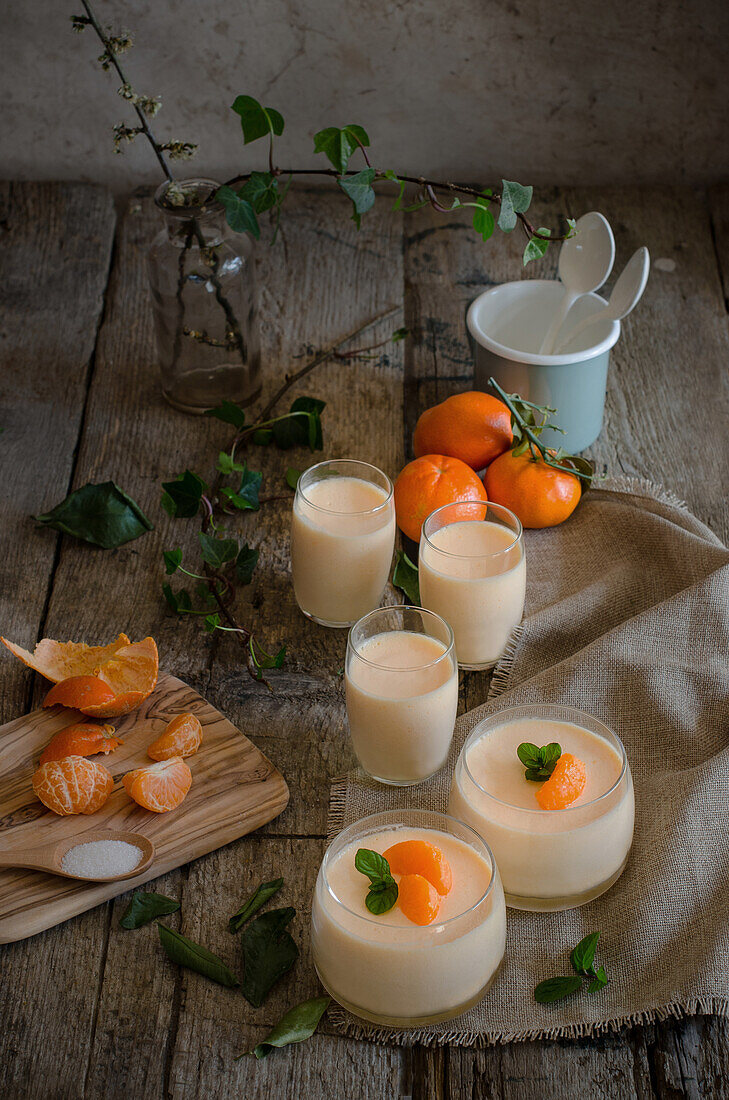 Blick von oben auf eine leckere Mandarinenmousse, garniert mit frischen Minzblättern, serviert in Glasbechern auf einem Holztisch