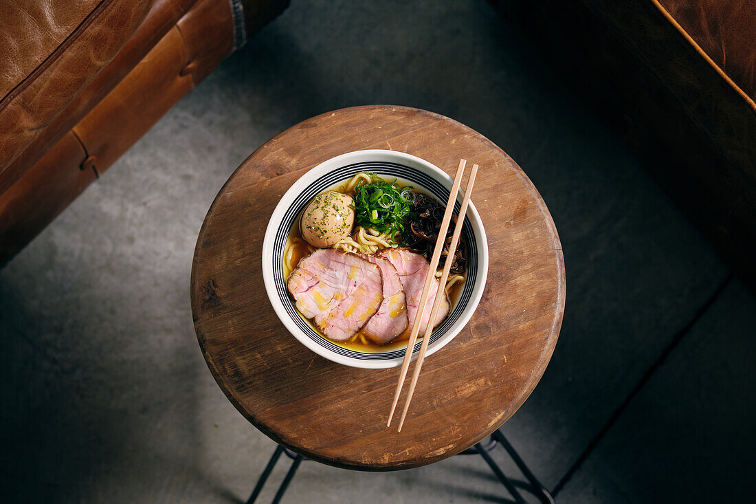 Top view of delicious traditional ramen soup in bowl with chopsticks served on round table
