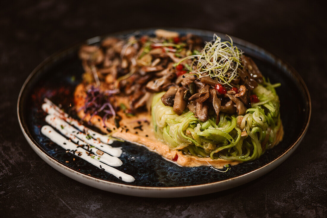 Yummy vegan dish with zucchini spaghetti and sauteed mushroom slices covered with red berries and alfalfa sprouts on dark background