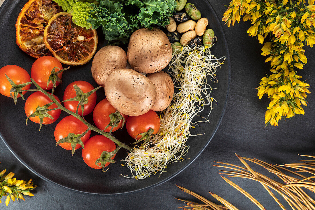 Top view of plate with bundle of fresh cherry tomatoes near cooked potatoes and sprouts on gray background with flowers