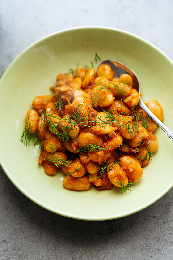 From above of delicious traditional Greek giant naked beans in tomato sauce served in plate on gray background in kitchen