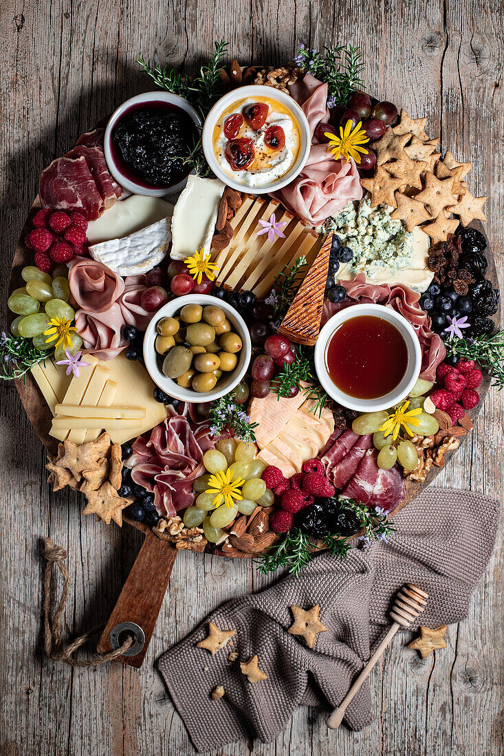 Ansicht von oben von Prosciutto mit verschiedenen Käsesorten auf einer Platte mit Beeren und Keksen auf einem Holztisch in der Küche