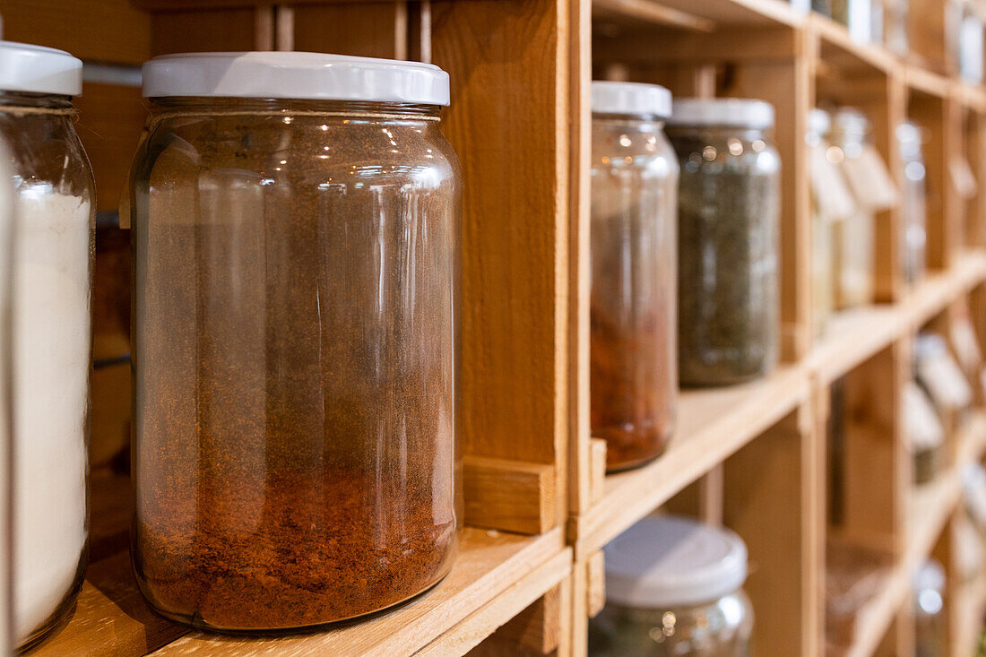 Glass jars placed on wooden shelves in modern shop with various seasonings for sale