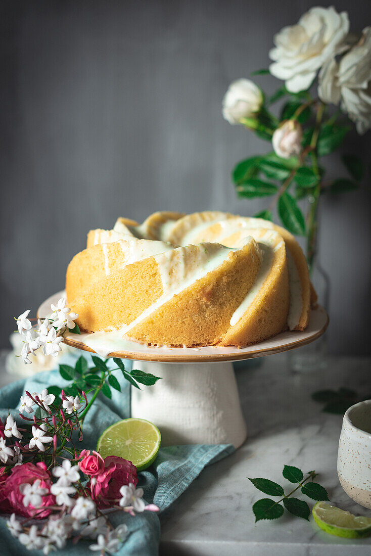 Tasty lime sponge cake served on white plate near flowers and lime slices