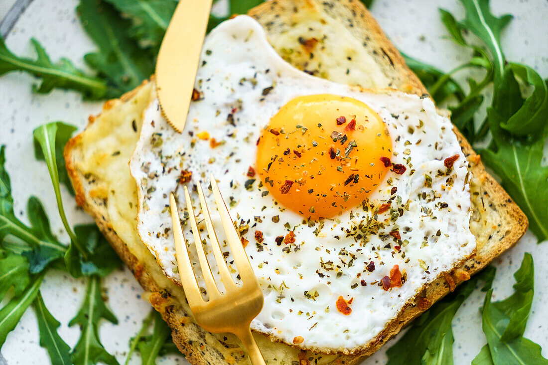 Von oben Toast mit Eiern und Käse und Rucolasalat auf einem Teller auf dem Tisch serviert