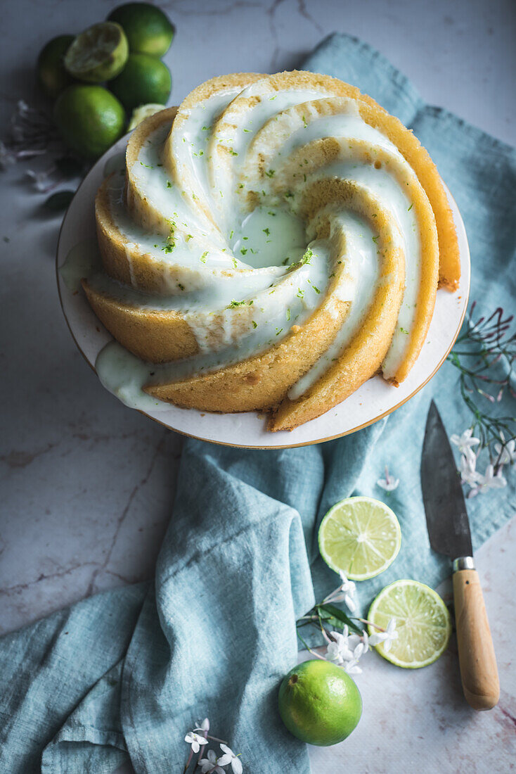 Top view of tasty lime sponge cake served on white plate near flowers and lime slices