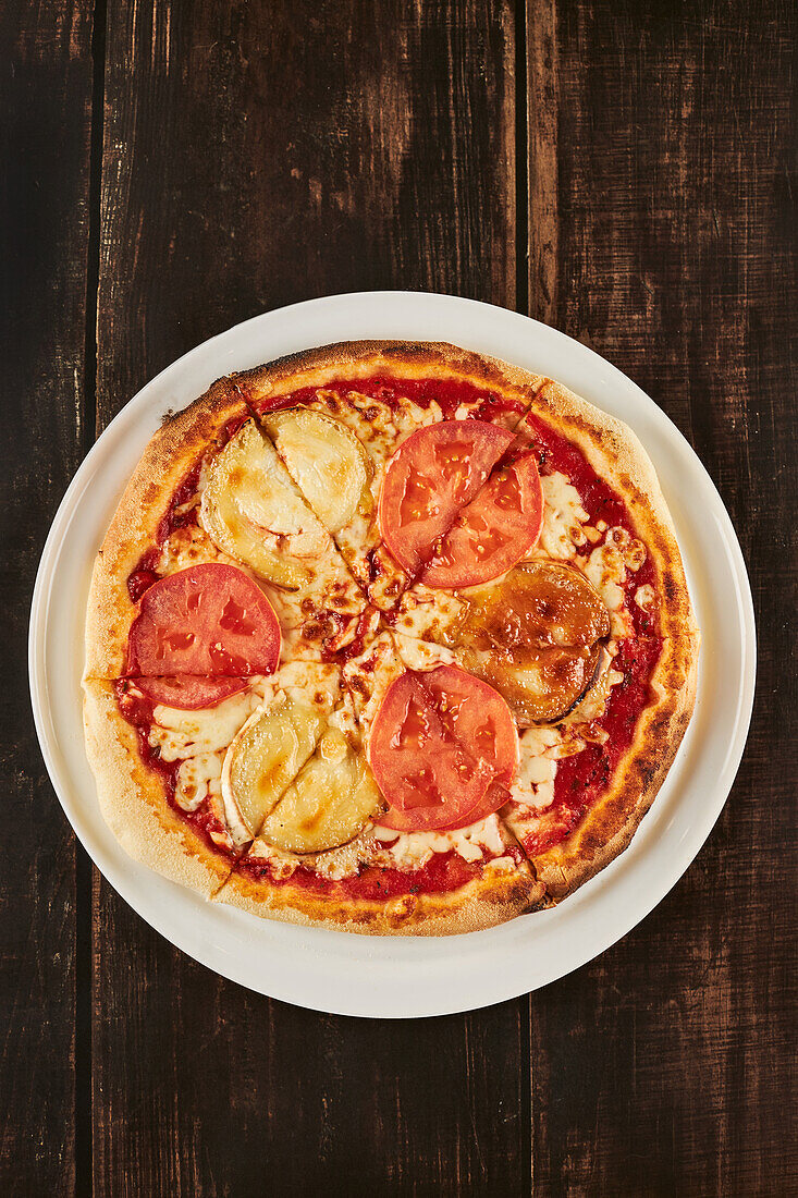 Draufsicht auf eine aufgeschnittene Pizza mit natürlichen Tomatenscheiben und Ziegenkäse auf einem Teller auf einem Holztisch in einer Pizzeria