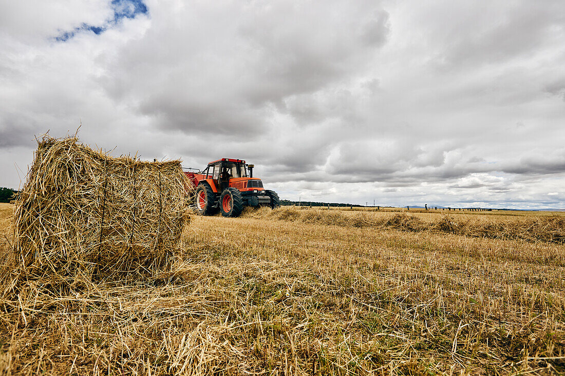 Dried hay roll and modern tractor placed on agricultural field in mountainous area in summer