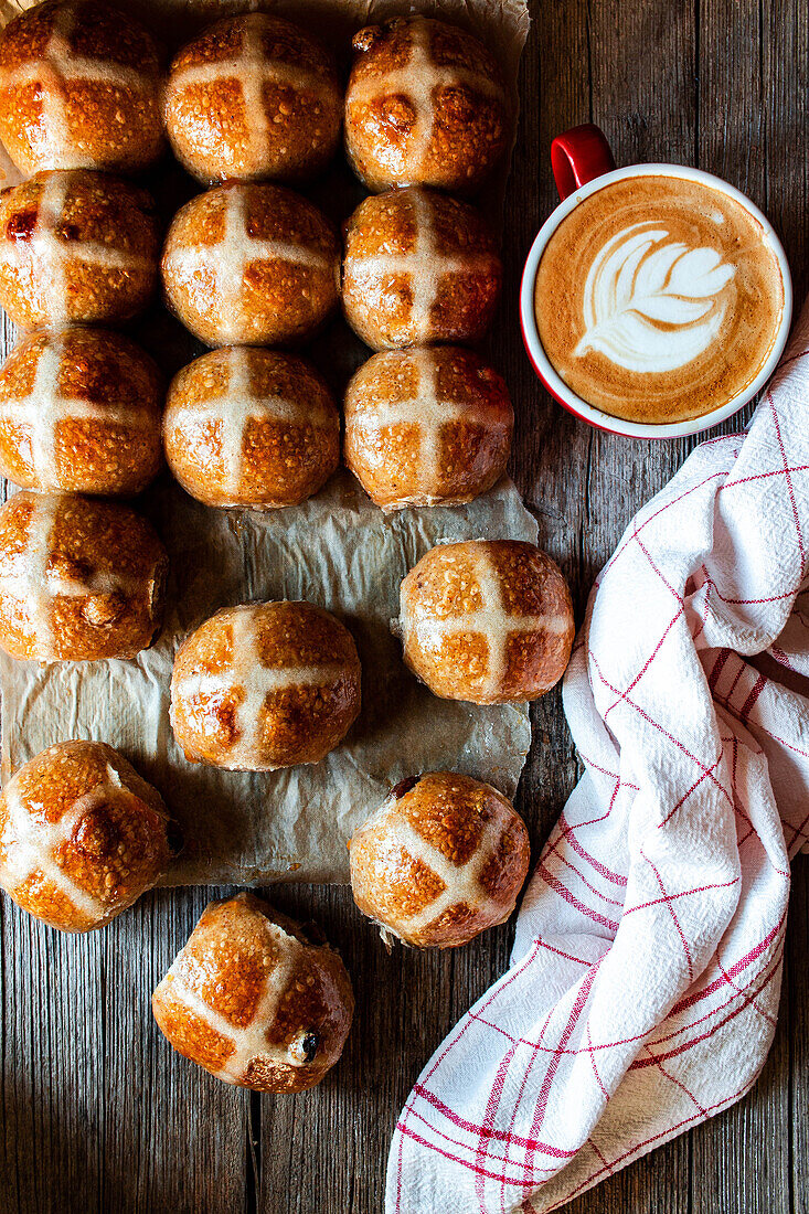 From above hand with appetizing freshly baked sourdough hot cross buns and mug of coffee on wooden table