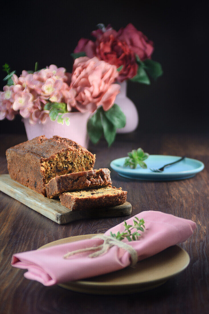 Still life of a sponge cake next to some pink vases with flowers on a table